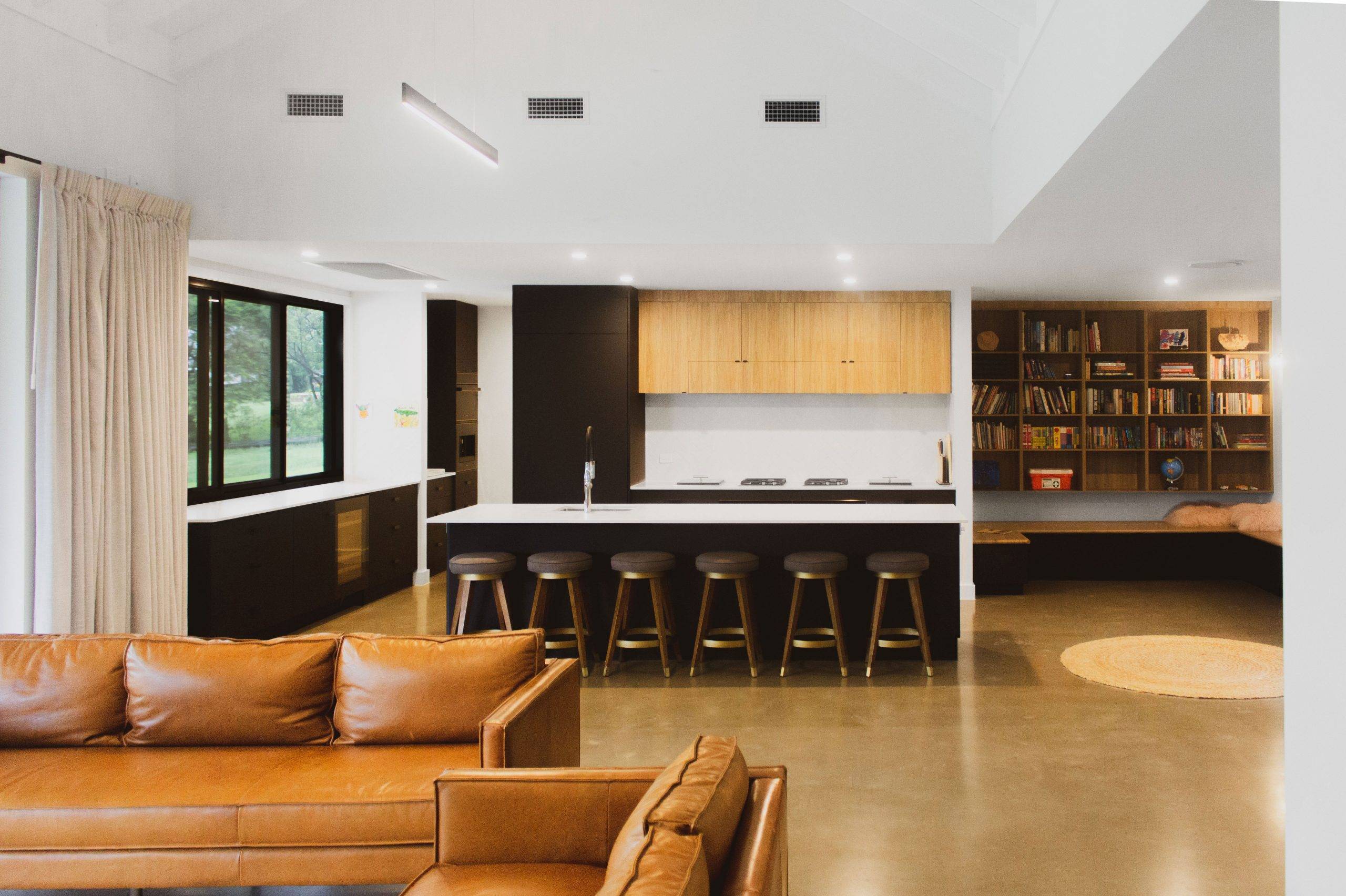 Cantwell St Architect designed contemporary farmhouse style home, High raked ceilings with exposed rafters, Large covered outdoor spaces, Minimalist material palette of polished concrete, stained timber, exposed brick and white paint.